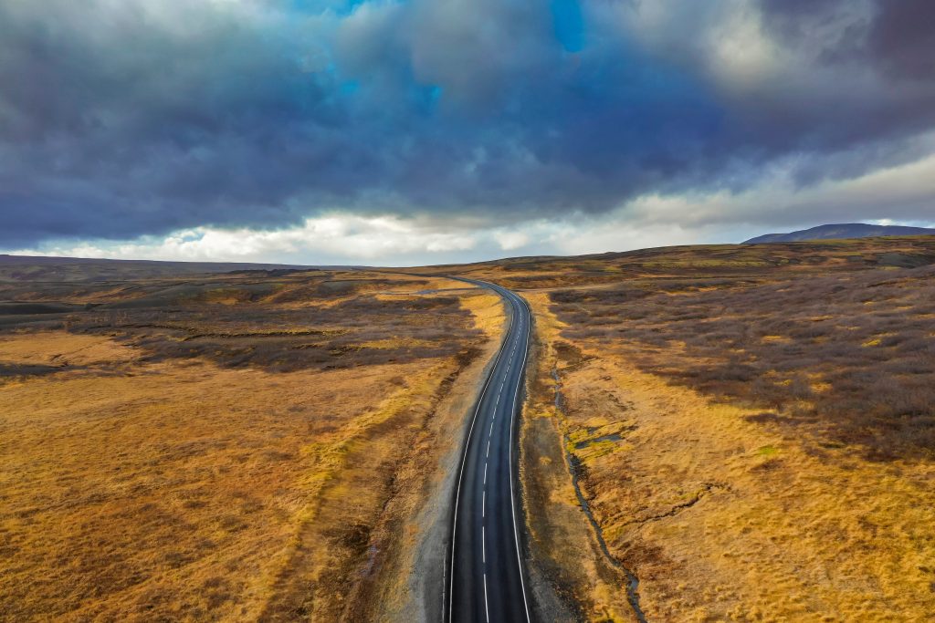 A beautiful view of a road surrounded by dry fields under the cloudy sky - Represents Raha's journey