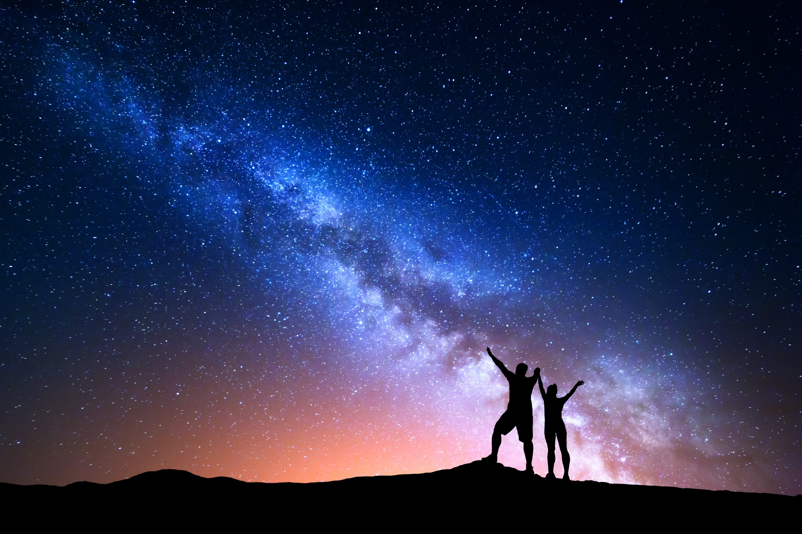 Milky Way. Colorful night sky with stars and silhouette of standing happy people with raised up arms on the hill. RahaWeb