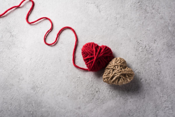 Red yarn heart shaped on the wall background - Represents Token of Love and Attraction article on RahaWeb