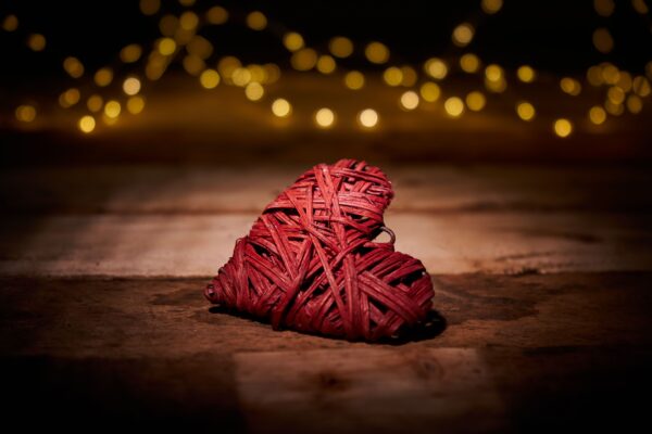 A woven heart on a wooden floor with bokeh in the background - Represents Token of Love and Attraction article on RahaWeb