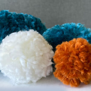 colorful handmade yarn pompoms by Raha are laying next to each other - Represents Yarn Pompoms article on RahaWeb