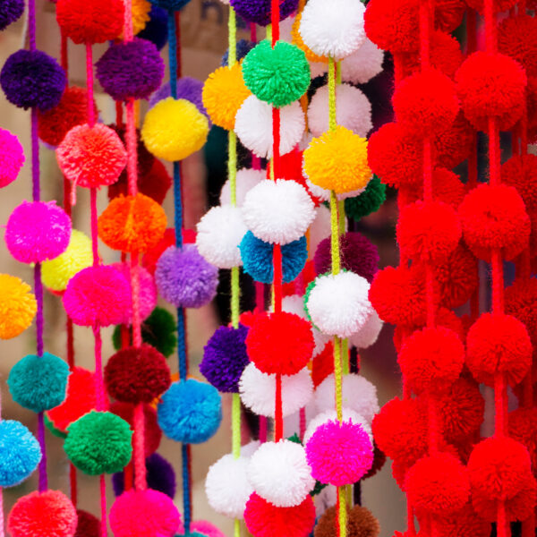 Colorful decorative pom-poms hanging from a wall - Represents Yarn Pompoms article on RahaWeb