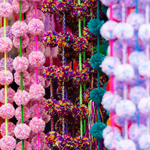 Colorful decorative pom-poms hanging from a wall - Represents Yarn Pompoms article on RahaWeb