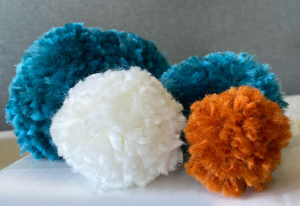 colorful handmade yarn pompoms by Raha are laying next to each other - Represents Yarn Pompoms article on RahaWeb